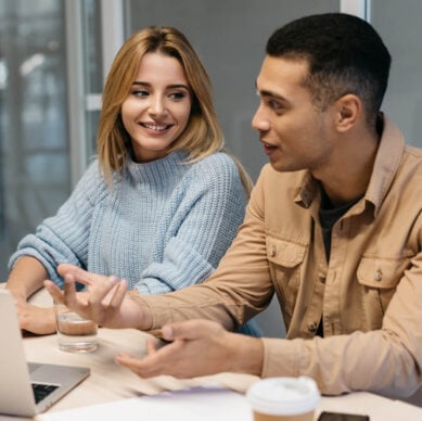 Two professionals discussing investment analysis strategies at a table with a laptop and coffee, reflecting collaboration in financial consulting.