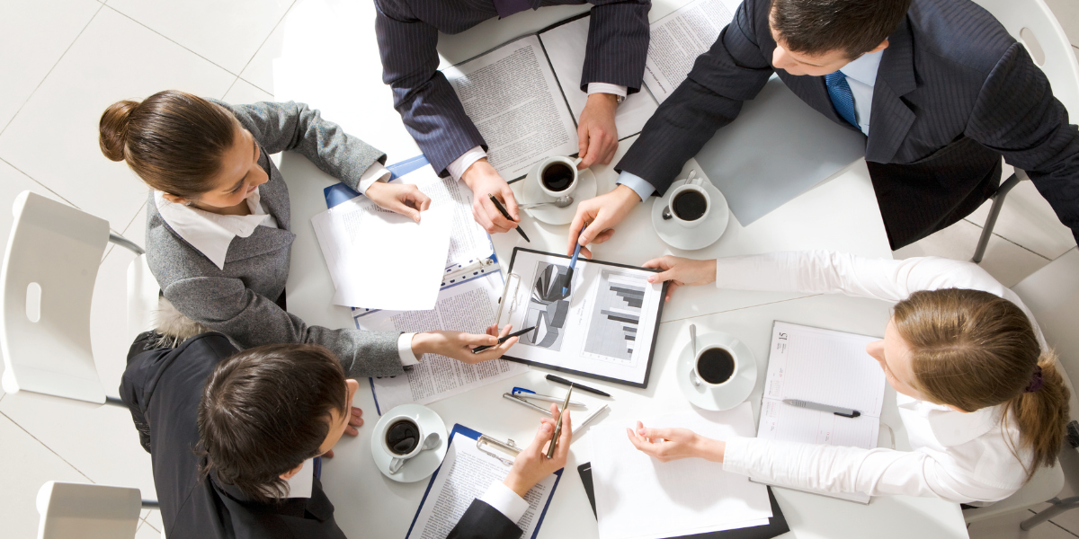 Group of professionals collaborating at a table, analyzing graphs and documents, with coffee cups, emphasizing leadership development and strategic planning in association management.